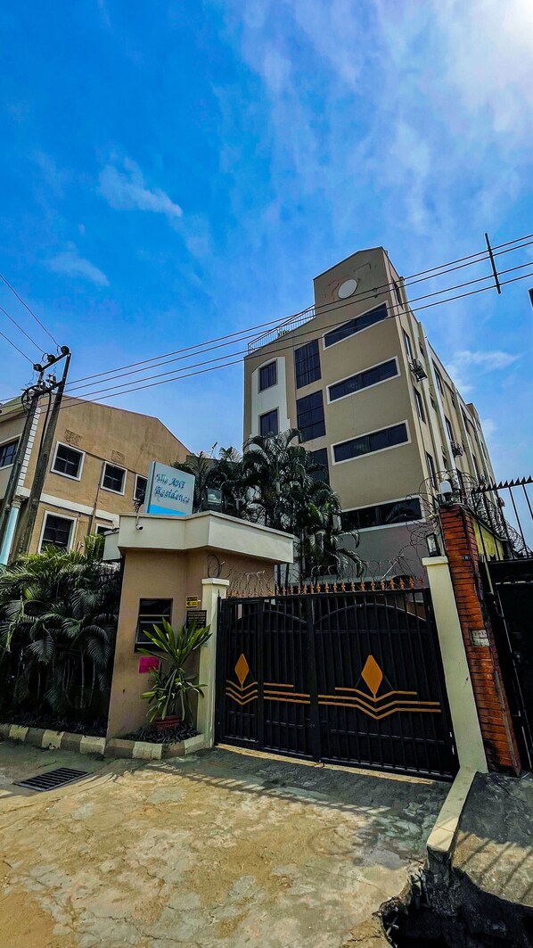 A hotel entrance with a gated driveway, a signboard, and a building with multiple floors.