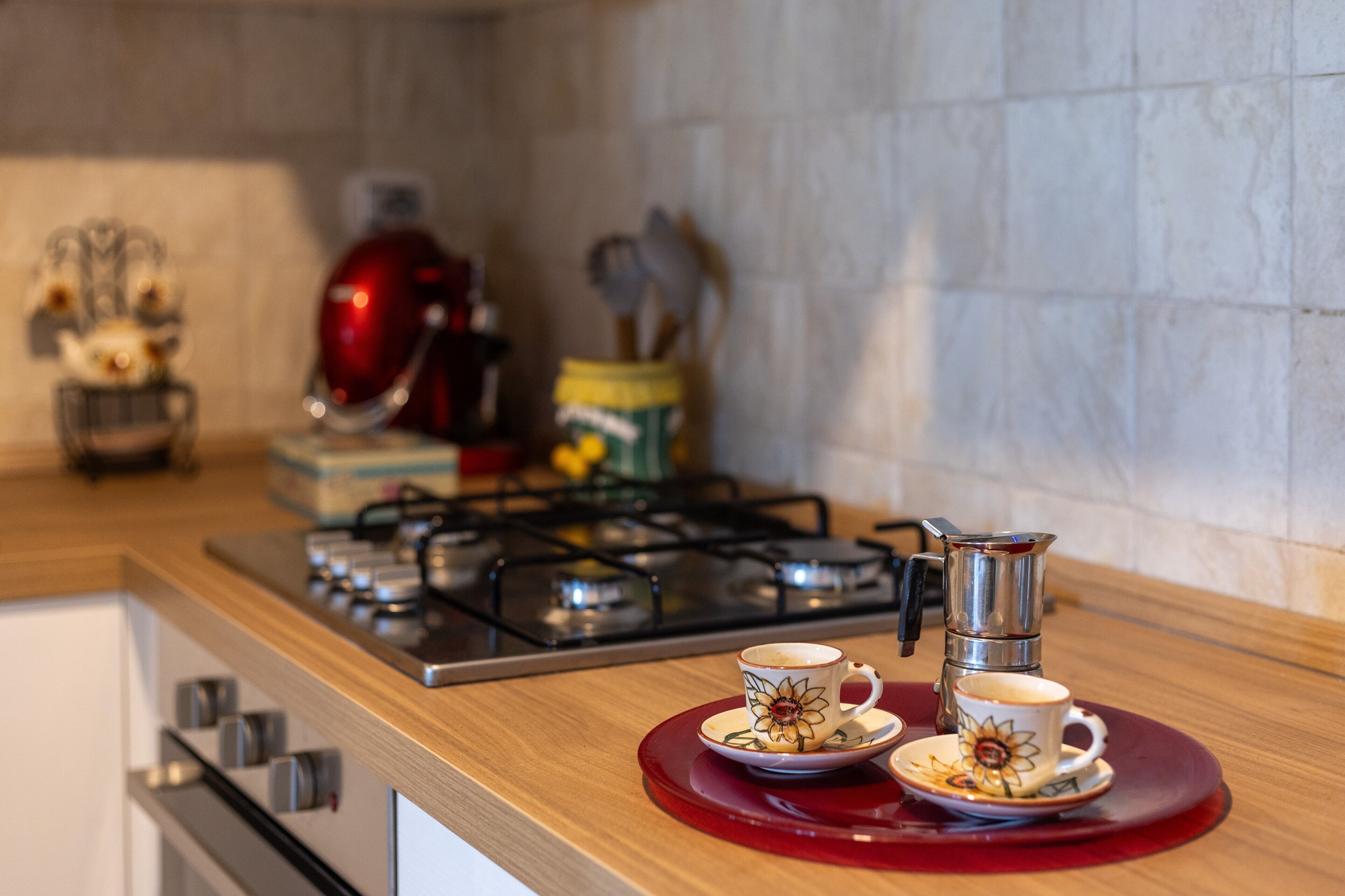 Un comptoir de cuisine avec une cuisinière à gaz, une machine à café et deux tasses sur un plateau rouge.