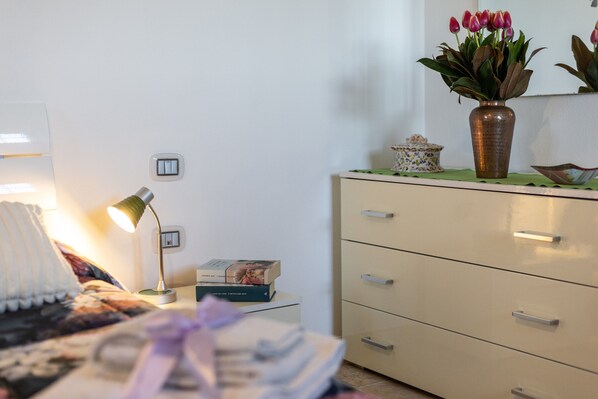 Quarto com cama, luminária de cabeceira, cômoda e um vaso com flores.