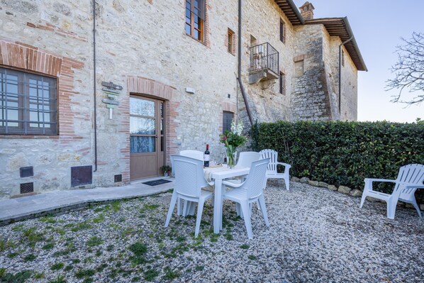 A stone building with a patio area featuring white plastic chairs and a table.