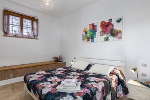 A bedroom with a bed, a window, artwork on the wall, and a bedside table.