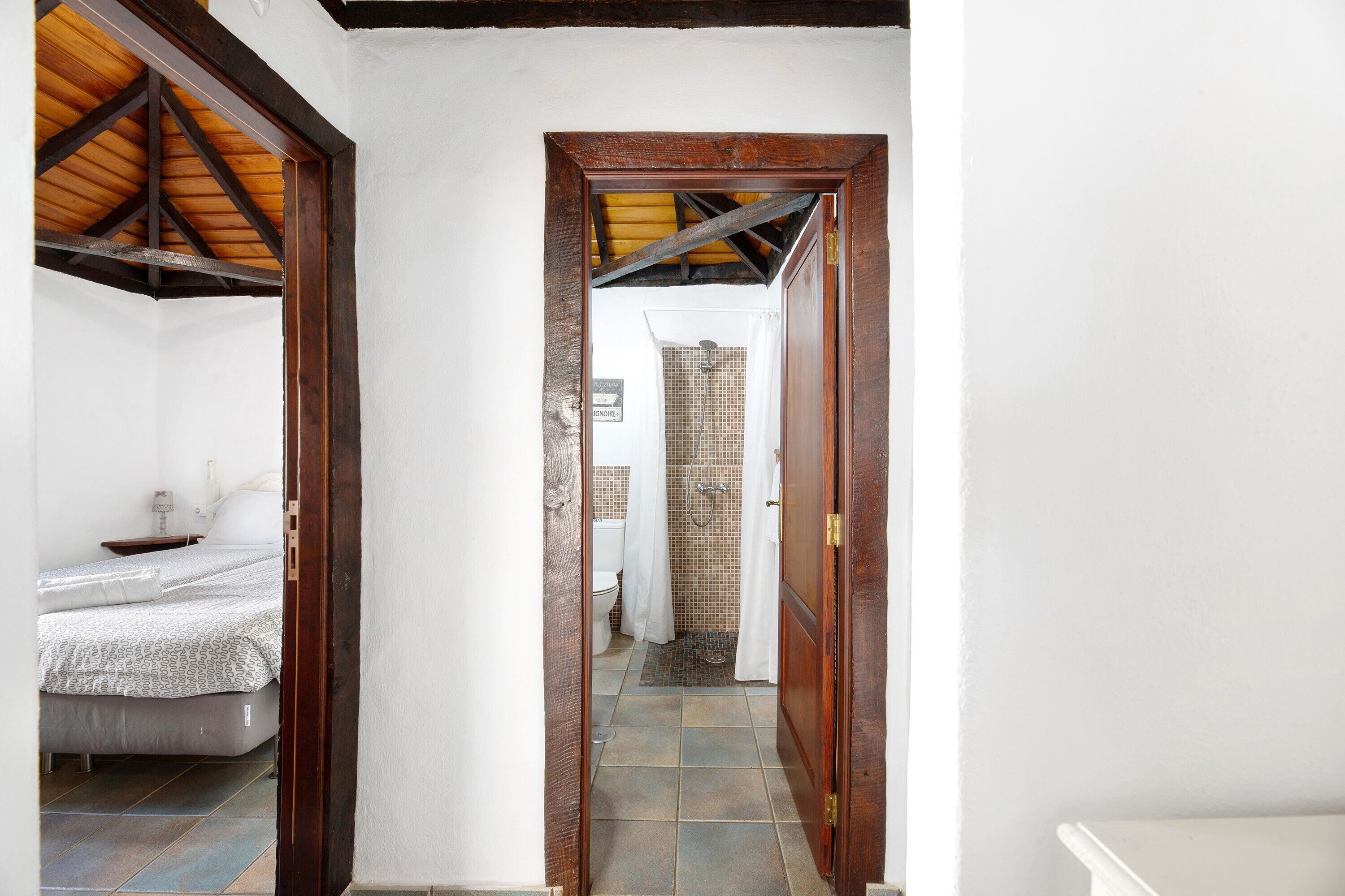 A narrow hallway leading to a bedroom with a bed and a bathroom with a shower.