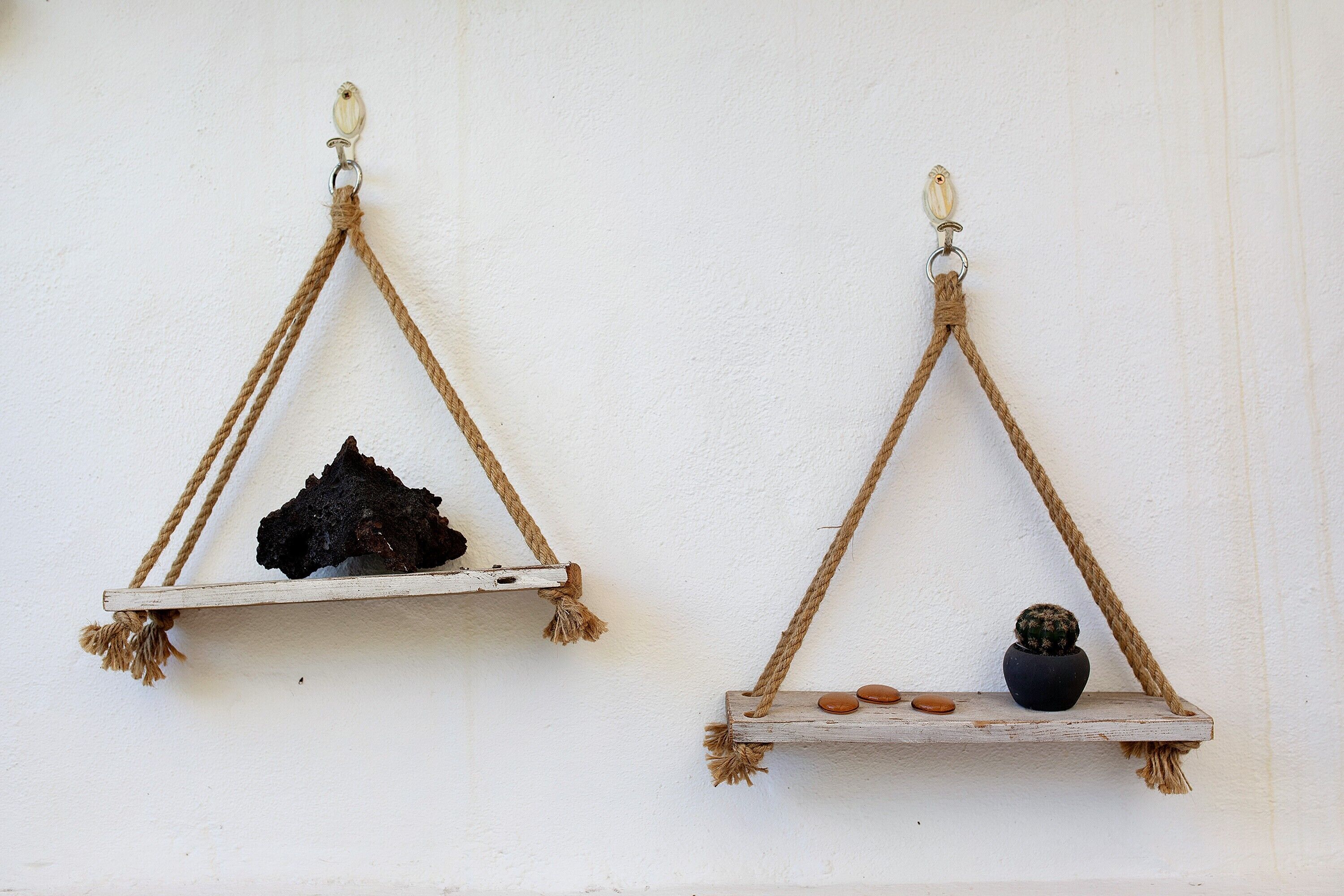 Two wooden triangular shelves suspended by ropes against a white wall.