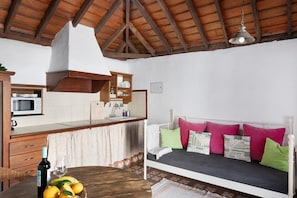 A room with a bed, a dining table with fruit, a bottle of wine, and a kitchen area.