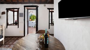 Ein Essbereich mit Holztisch, einer Weinflasche und Gläsern. An der Wand ist ein Fernseher angebracht und es gibt einen Ausblick ins Freie.