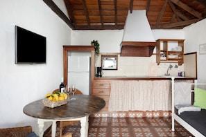 Une pièce comprenant un lit, une table avec des fruits et des verres à vin, une télévision, un coin cuisine et un plafond en bois.