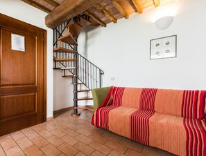 Een trap met houten leuningen, een houten deur, een bank met een gestreept plaid en een wandlamp.