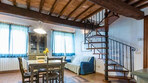 A dining area with a wooden table and chairs, a sofa, and a staircase. - Holiday Home 'Podere Simonetta - A2' with Shared Pool, Private Terrace and Wi-Fi (Cecina)