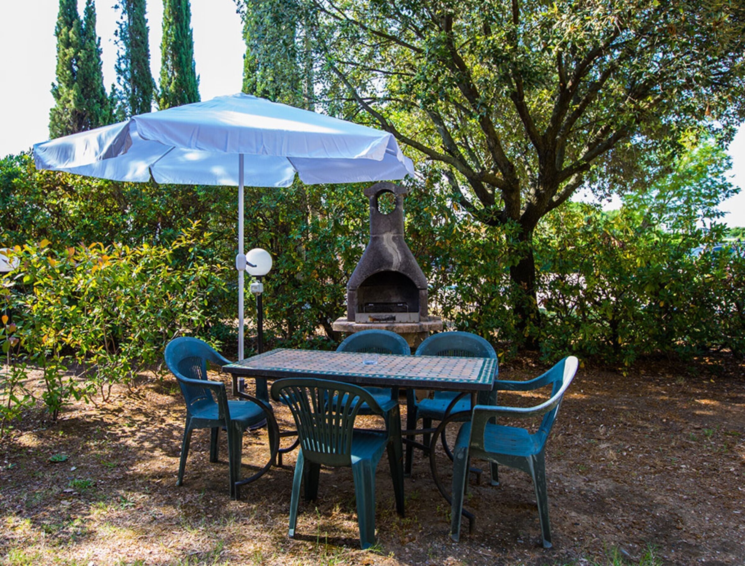 An outdoor patio with a table and chairs, a stone oven, and a large umbrella.