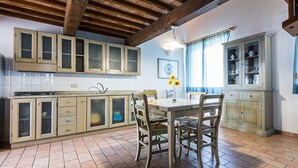 A kitchen with wooden cabinets, a dining table with chairs, and a tiled floor. - Holiday Home 'Podere Simonetta - A2' with Shared Pool, Private Terrace and Wi-Fi (Cecina)
