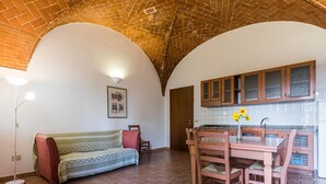 A cozy room with a sofa, a dining table with chairs, a kitchen area with cabinets, and a tiled floor. - Holiday Home 'Podere Simonetta - A5' with Shared Pool, Private Terrace and Wi-Fi (Cecina)