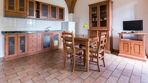 A kitchen with wooden cabinets, a dining table with chairs, a TV on a stand, and a brick ceiling. - Holiday Home 'Podere Simonetta - A5' with Shared Pool, Private Terrace and Wi-Fi (Cecina)