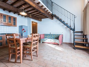Une cuisine avec des meubles en bois, une table à manger avec des chaises, un canapé et un escalier.