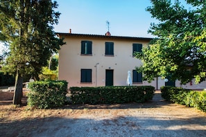 A two-story building with a beige facade, green shutters, and a gravel driveway. - Holiday Home 'Podere Simonetta - A9' with Shared Pool, Private Terrace and Wi-Fi (Cecina)