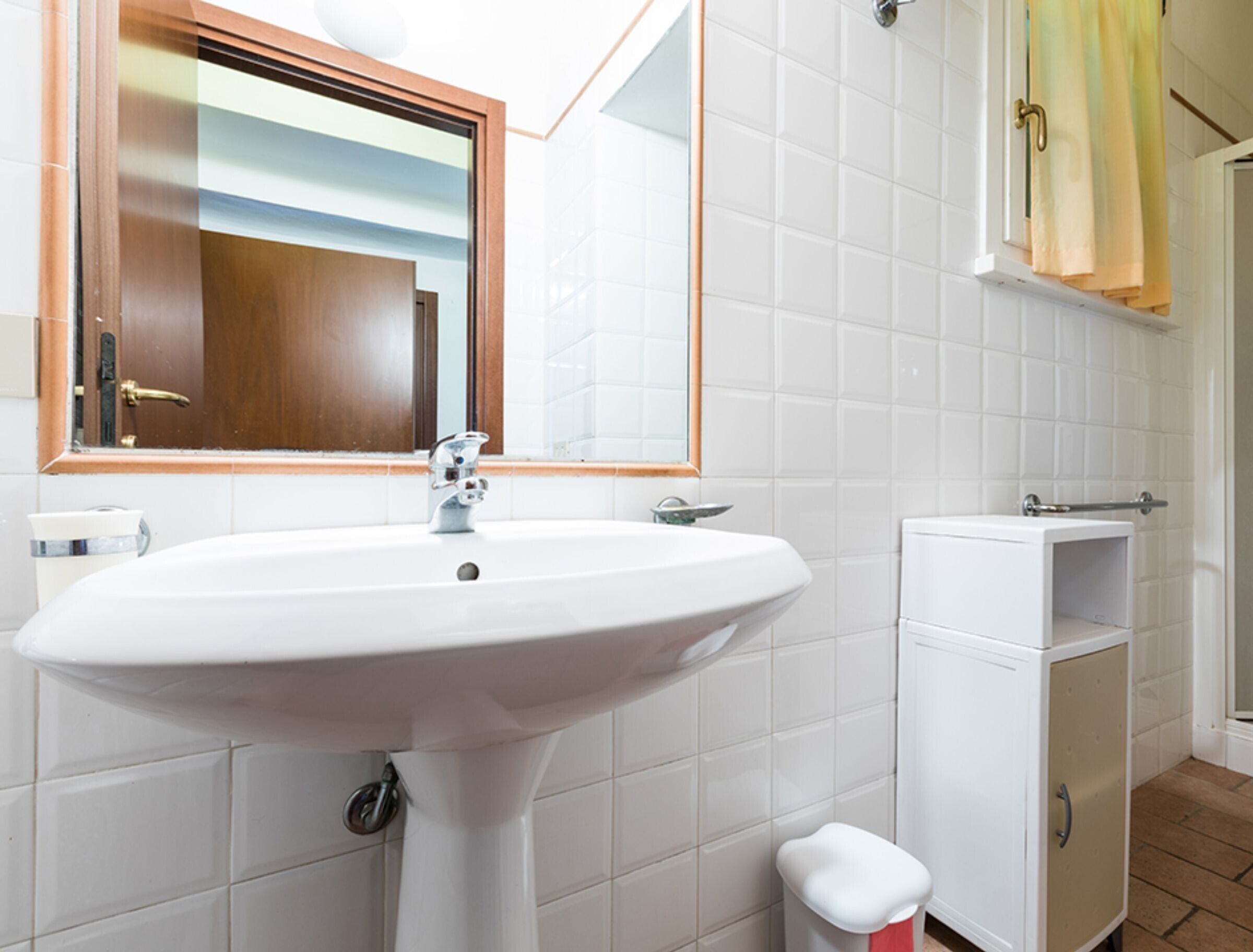 Une salle de bain avec un lavabo blanc, un miroir, un porte-serviettes et un meuble de rangement.