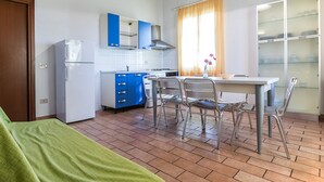 A compact kitchen with a dining area, a refrigerator, cabinets, and a window with curtains. - Holiday Home 'Podere Simonetta - A13' with Shared Pool, Shared Garden and Wi-Fi (Cecina)