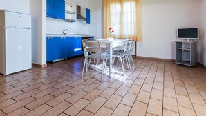 Une cuisine avec des meubles de rangement bleus, un réfrigérateur blanc, une table à manger avec des chaises et un meuble pour la télévision.