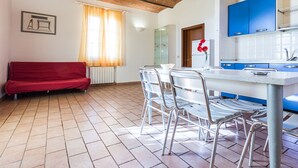 Un coin repas avec une table et des chaises, un canapé rouge, une fenêtre avec des rideaux et un espace cuisine avec des placards bleus.