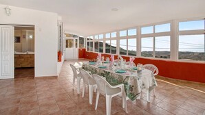 Un coin repas avec une table dressée pour quatre personnes, des chaises blanches et de grandes fenêtres donnant sur la campagne.