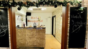 Ein Hotel-Empfangsbereich mit einer Steintheke, einem Schild mit der Aufschrift 'Hotel Neuendorf' und 'Hotel 9-ehop' sowie einem 'RECEPTION'-Schild über der Tür.