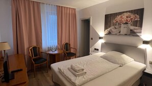 Ein Hotelzimmer mit einem Bett, zwei Stühlen, einem Schreibtisch mit Lampe und einem Bild an der Wand.