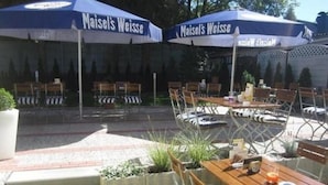 Ein Außenbereich mit Tischen und Stühlen unter blauen Sonnenschirmen, auf denen "Maisel's Weisse" steht.