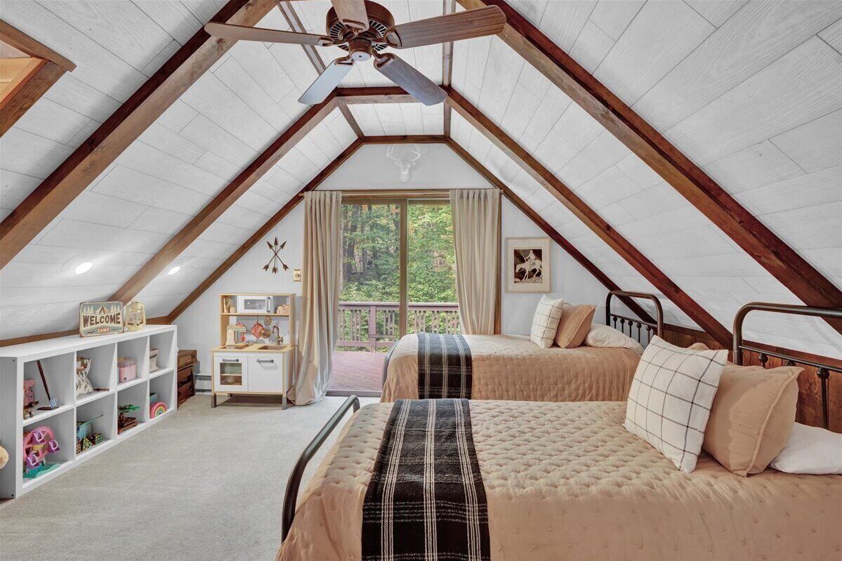 A cozy attic bedroom with a sloped ceiling, a bed with a plaid bedspread, a wooden desk, and a bookshelf.