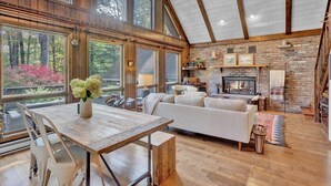 A spacious living room with a fireplace, wooden beams, large windows, and a dining area.