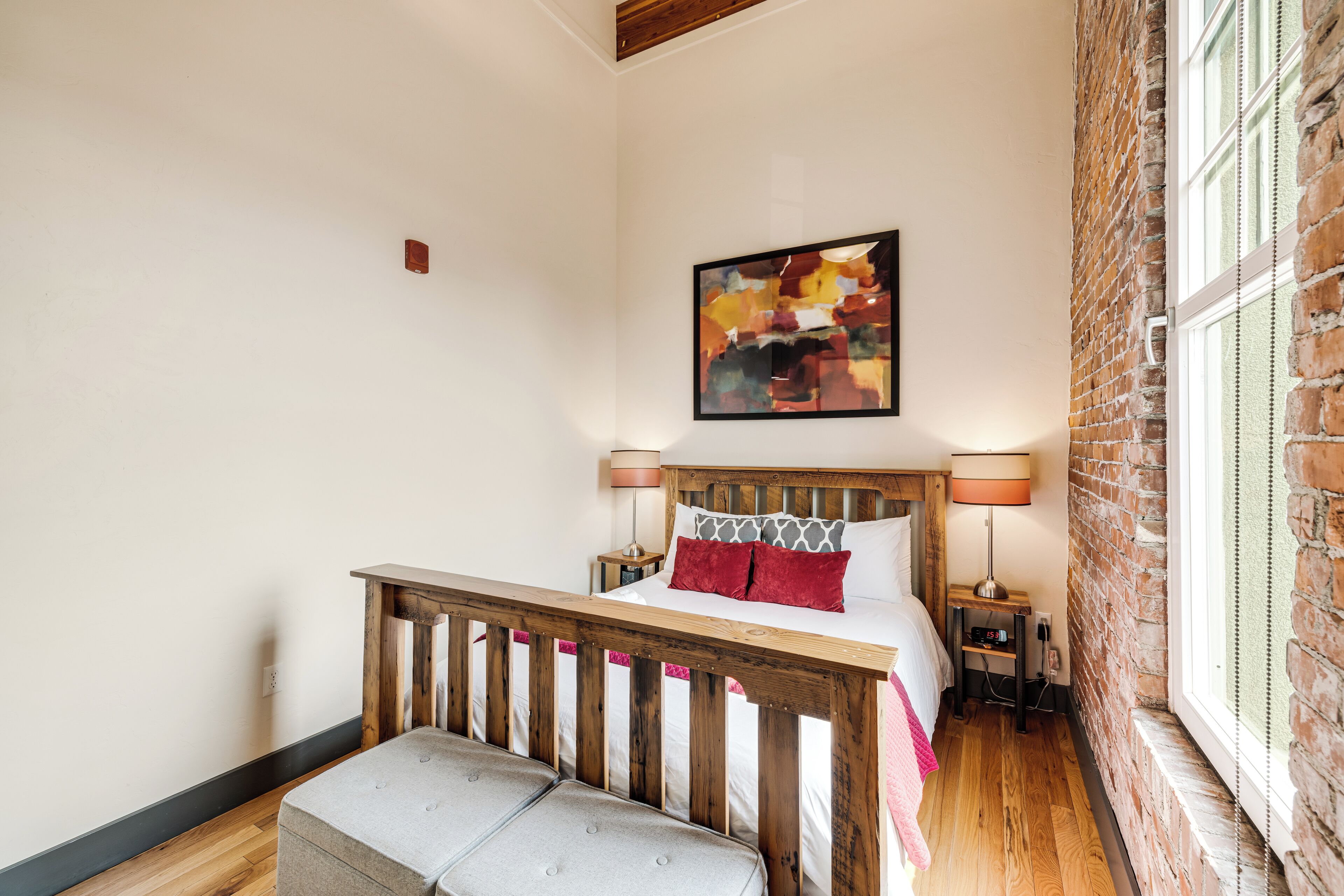 Une chambre à coucher avec un lit en bois, un banc, une table de chevet, une lampe et un mur en briques.