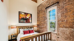 Una habitación con una cama de madera, una pared de ladrillo, una ventana y un cuadro en la pared.