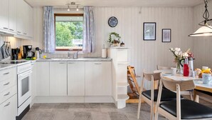 Eine moderne Küche mit weißen Schränken, einem eingebauten Backofen und einem Essbereich mit Holztischen und -stühlen.