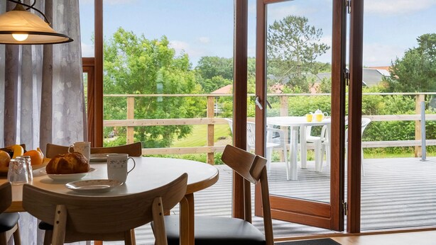 Ein Essbereich mit Tisch und Stühlen, ein Fenster mit Blick auf Grünflächen und eine Tür, die zu einer Außenterrasse führt.