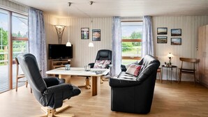 Ein modernes Wohnzimmer mit Fernseher, Ledersesseln, einem Esstisch und Blick auf Grünflächen.