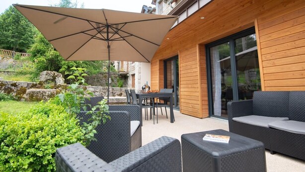 Terrassa exterior amb moble de vimet, taula i un para-sol gran.