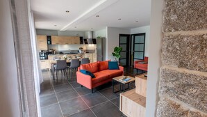 Un saló modern amb un sofà i una taula de centre, una zona de menjador amb cadires, i una cuina amb armaris de fusta i una estufa.