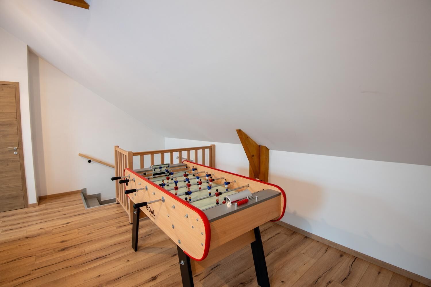 A foosball table in a room with wooden flooring and a staircase.