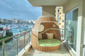 Un balcon agrémenté d’un fauteuil en osier original et offrant une vue sur un port de plaisance.