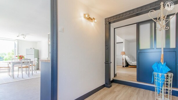 Un intérieur moderne avec une porte bleue, un coin repas comprenant une table et des chaises, et un couloir avec un porte-parapluie bleu.