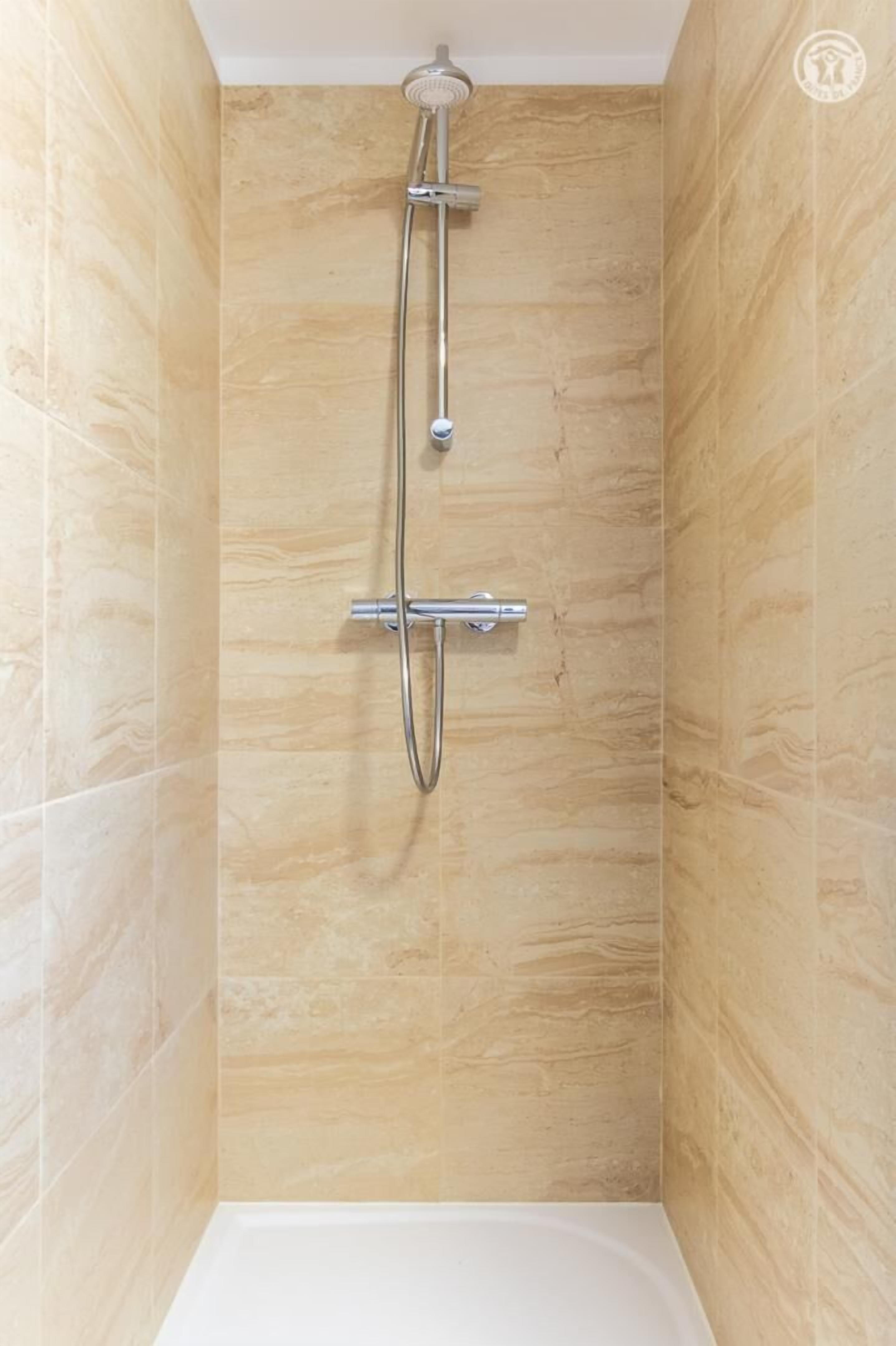 Une douche équipée d’un pommeau de douche à main et d’un pommeau de douche fixe fixé au mur, dans une pièce carrelée.