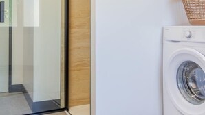Un espace buanderie comprenant un lave-linge, un meuble en bois et une porte en verre donnant accès à une douche.