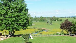Een grasveld met een beekje, bomen en een speeltuin.