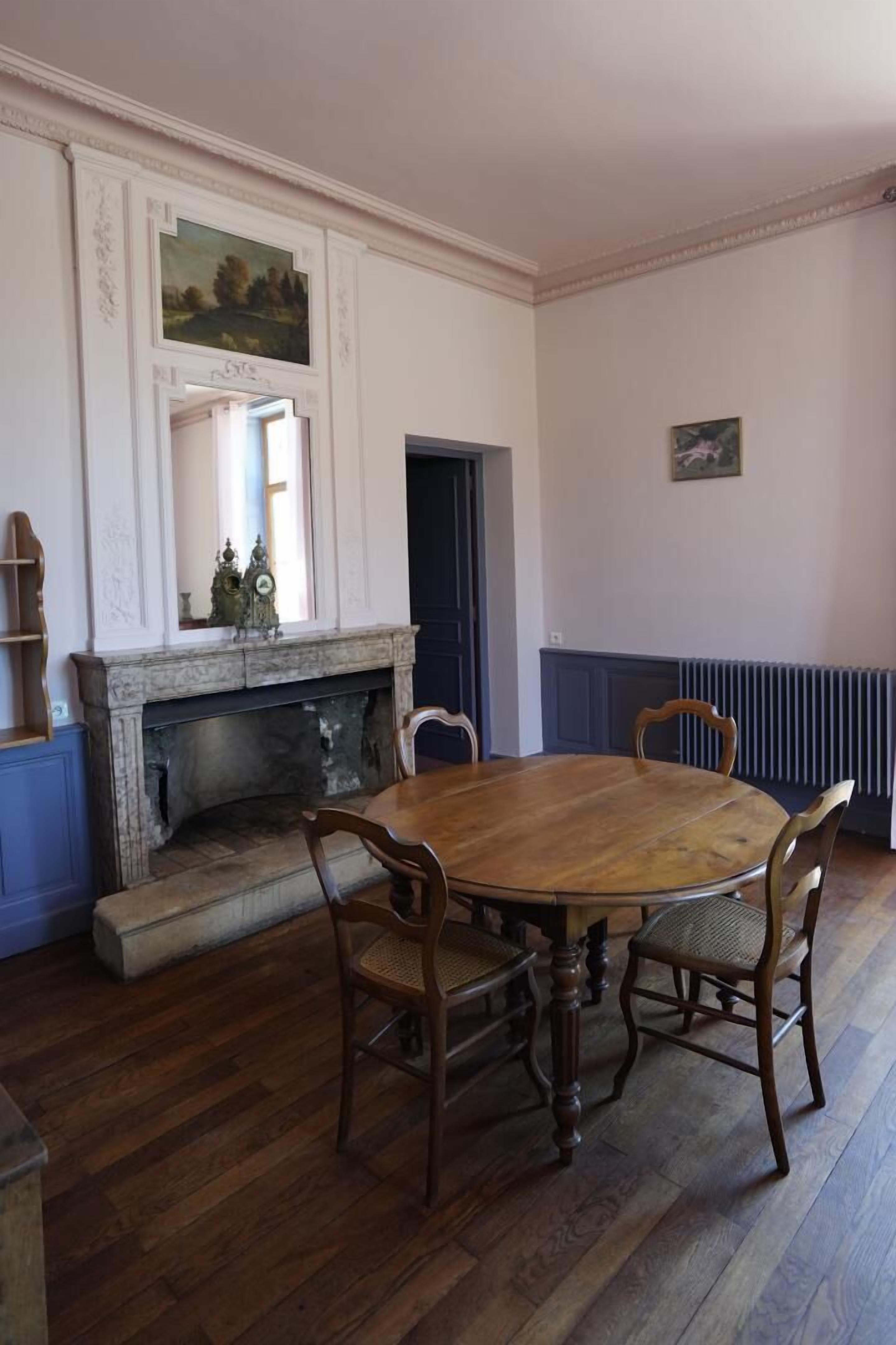 A dining room with a wooden table and chairs, a fireplace, and a mirror above it.