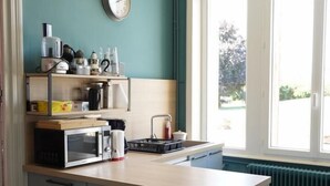 Een kleine keuken met een magnetron, waterkoker en diverse keukenbenodigdheden op een plank.