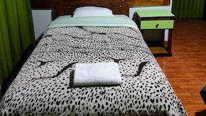 Una cama con una colcha de estampado de leopardo, un cabecero de madera, una mesita de noche verde y un marco de fotos en la pared.