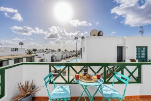 A rooftop terrace with a pool, turquoise chairs, and a table with breakfast.