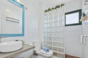 A bathroom with a round sink, a toilet, a mirror with a blue frame, and a window with a view of the outside.