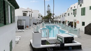 Un espace piscine comprenant des chaises longues, une piscine et des palmiers.