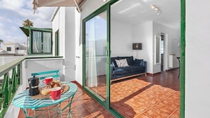 Un balcon avec une table préparée pour le petit-déjeuner, une porte-fenêtre coulissante donnant sur un espace de vie avec un canapé, et une vue sur l’extérieur.