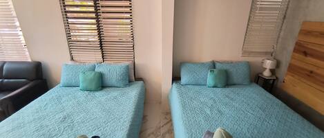 Two twin beds with matching blue bedding, a ceiling air conditioner, and a wooden headboard.