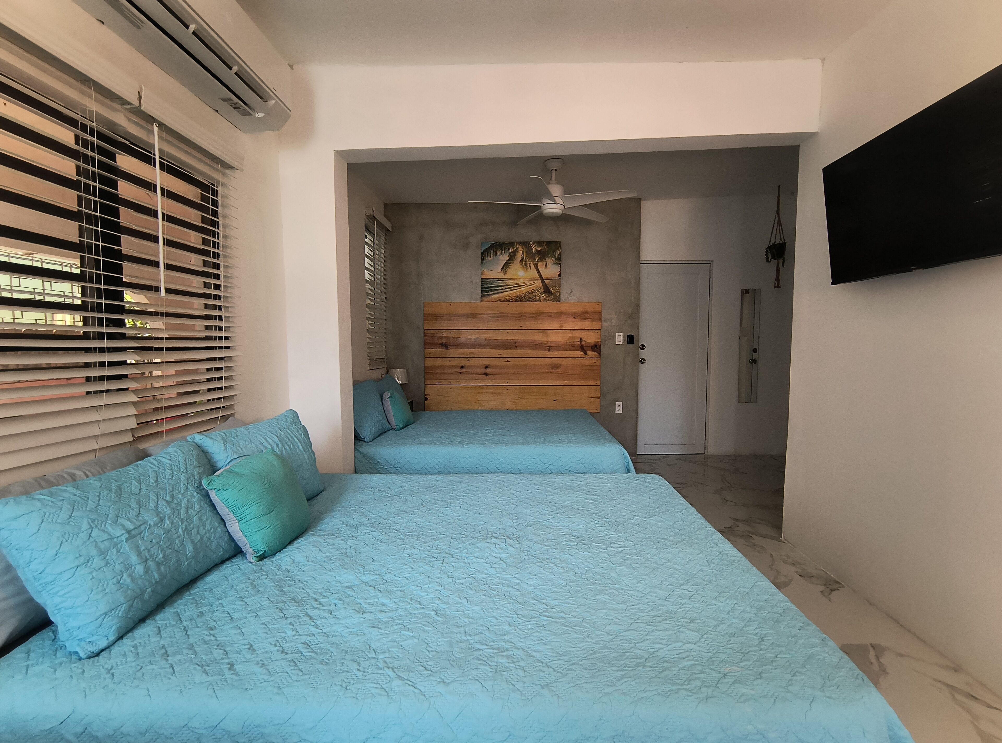 Quarto com uma cama, ventilador de teto e televisão fixada na parede.